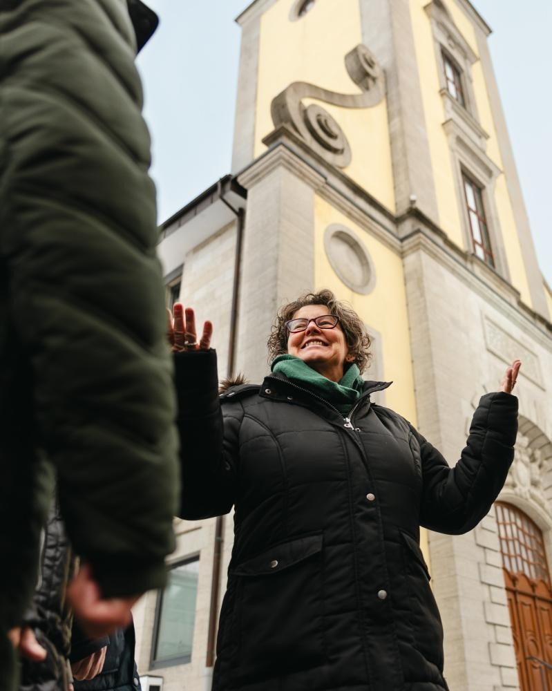 Stadtführerin steht lächeld vor dem Rathausturm und spricht mit einer Menschengruppe