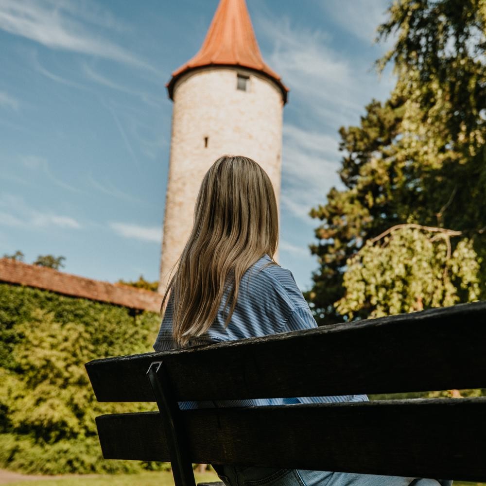Junge Frau sitzt auf einer Bank und blickt auf den Diebsturm
