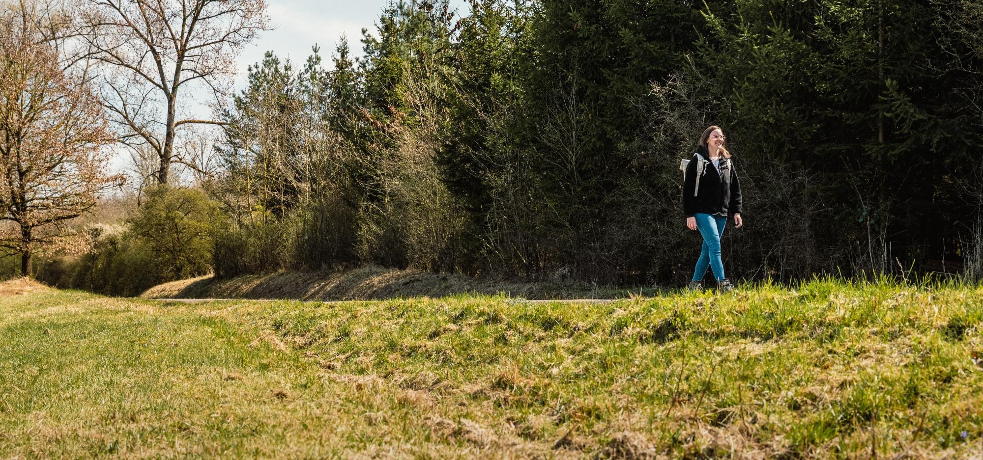 Eine Frau mit Rucksack wandert am Waldrand entlang