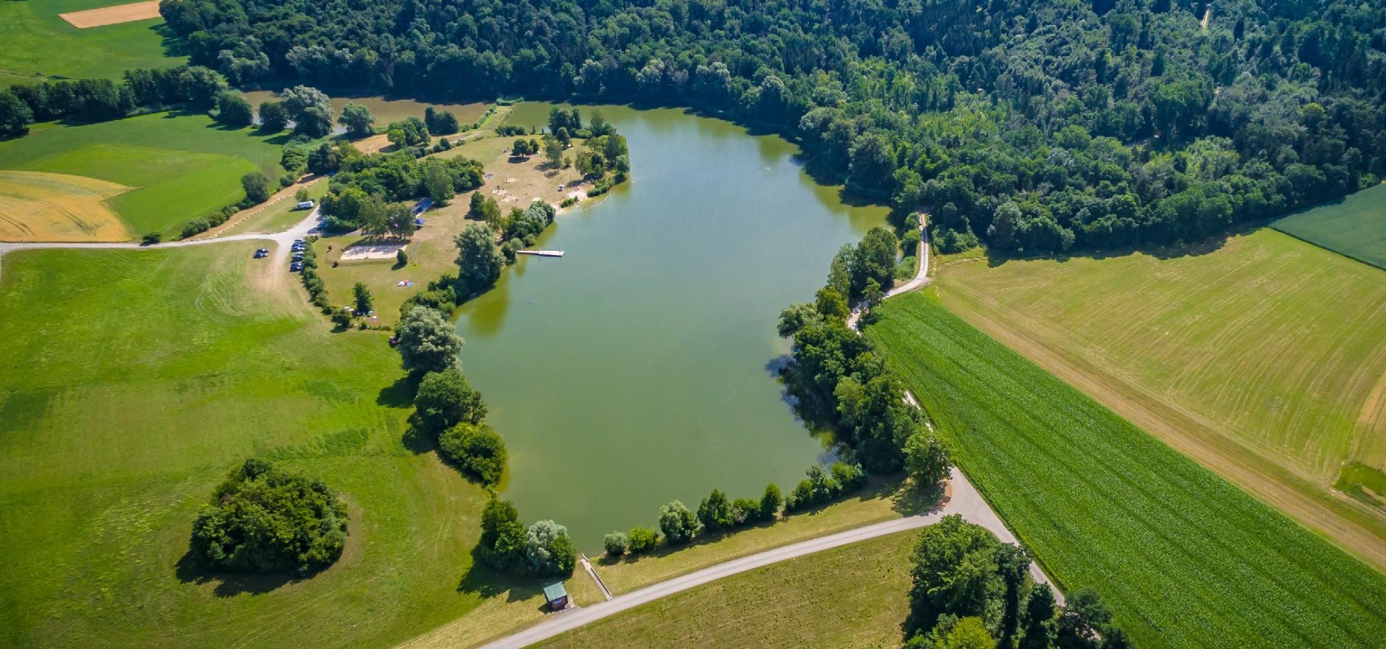 Luftaufnahme des Degenbachsees, der von Feldern und Wald umrandet ist