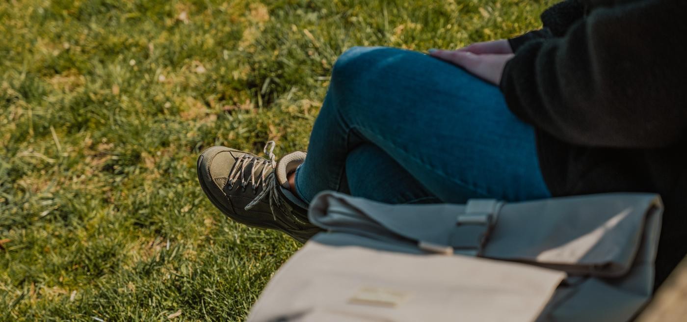 Frau mit Wanderschuhen sitzt auf einer Bank, neben ihr liegt ein Rucksack